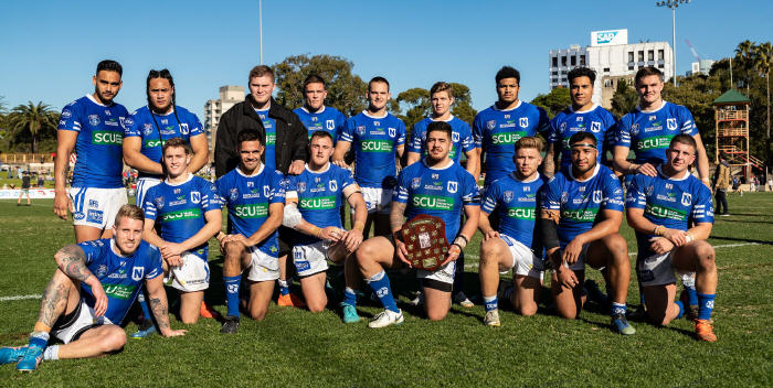 The Newtown Jets have retained possession of the Frank Hyde Shield for another year by virtue of being the current holders. This year’s series was tied with two drawn games, and in 2017 the two clubs each won one game and lost one game, and had identical points for and against! The full team complement is:
Standing, from left to right: Briton Nikora, Charlton Schaafhausen, Daniel Vasquez, Kurt Dillon, Matt Evans, Blayke Brailey, Malakai Houma, Sosaia Feki, Kyle Flanagan. In front, from left to right: Aaron Gray, Jack A. Williams, Will Kennedy, Jimmy Jolliffe, Braden Uele (Captain), Lachlan Stein, Ava Seumanufagai, Billy Magoulias. Photo: Mario Facchini, mafphotography
